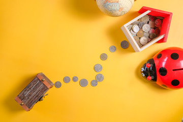 Ladybug piggy bank surrounded by coins and mini house on yellow background