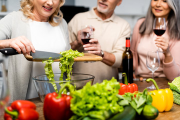 cropped view of woman adding lettuce to bowl and her friends holding wine glasses