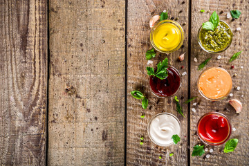 Set of sauces in small bowls - ketchup, mayonnaise, mustard, bbq sauce, pesto, classic burger sauce, with spices and herbs in. Wooden background copy space top view