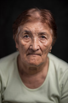 Portrait Of An Old Woman Against A Dark Background. Photographed Close-up.