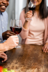 cropped view of smiling multicultural friends clinking with wine glasses in kitchen
