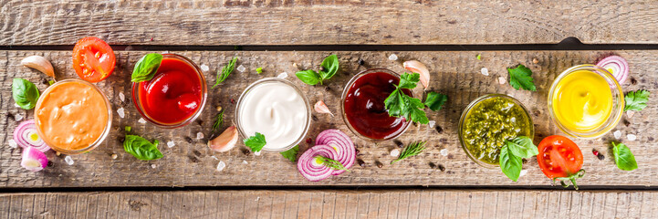 Set of sauces in small bowls - ketchup, mayonnaise, mustard, bbq sauce, pesto, classic burger sauce, with spices and herbs in. Wooden background copy space top view