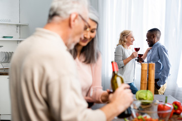 selective focus of african american man talking with smiling friend in kitchen