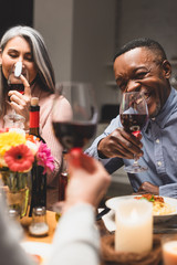 selective focus of smiling asian woman and african american man holding wine glasses during dinner