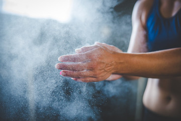 Female fitness model clapping hands with talcum powder in a gym before weight training