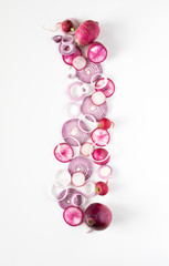 A top down view of a vertical abstract arrangement of overlapping red onion, daikon and radish slices all in a line.