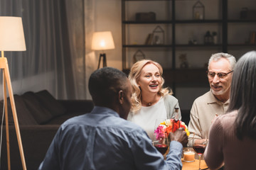 selective focus of smiling man and woman talking with multicultural friends during dinner