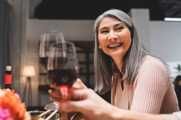 smiling and attractive Asian woman clinking with friend during dinner