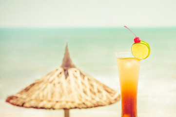 Long Island cocktail with fruits decoration at tropical ocean beach with umbrella. Vintage style, hipster colors image with copy space for party invitation text