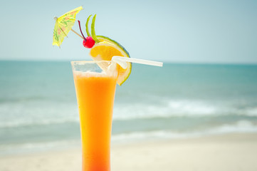 Tequila sunrise cocktail with fruits and umbrella decoration at tropical ocean beach. Vintage style, hipster colors image with copy space for party invitation text