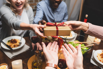 cropped view of multicultural man and woman giving present to friends during dinner