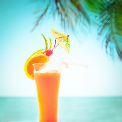 Tequila sunrise cocktail with fruits and umbrella decoration at tropical ocean beach with palm trees. Vintage style, hipster colors image with copy space for party invitation text