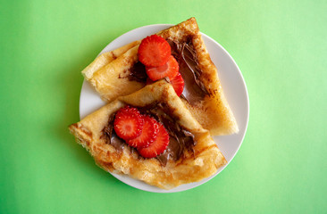 Fresh pancakes with chocolate paste and strawberry on green background. Russian style pancakes for Pancake Week. 