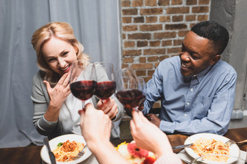 cropped view of friends clinking with caucasian woman and african american man during dinner