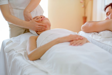 Thai masseuse do face massage for  young beautiful girl who lie and look up on bed in spa room.