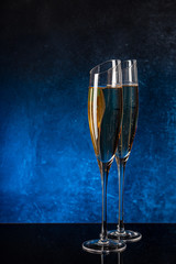 Two glasses with champagne on a black mirror surface. Blue background Concrete wall. Black glass. Crystal glass