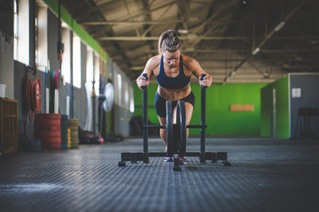 Female fitness model pushing a sled in a cross fit gym.