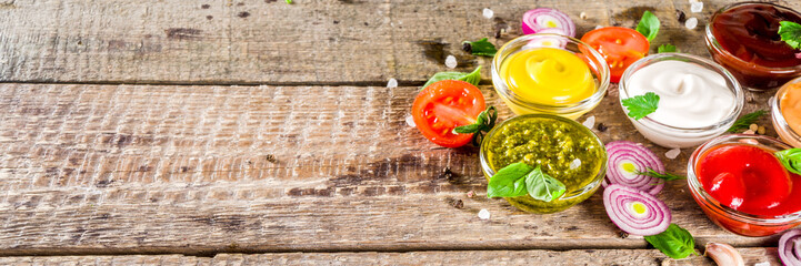 Set of sauces in small bowls - ketchup, mayonnaise, mustard, bbq sauce, pesto, classic burger sauce, with spices and herbs in. Wooden background copy space top view