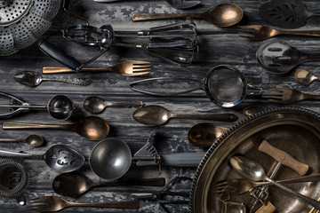 Top down view of an abstract arrangement of antique utensils and cutlery against a dark background.