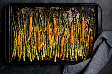 A top down view of a baking sheet with oven roasted asparagus and baby carrots drizzled with sauce.