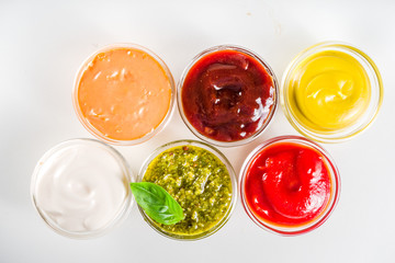 Set of sauces in small bowls - ketchup, mayonnaise, mustard, bbq sauce, pesto, classic burger sauce, with spices and herbs in. White background copy space top view