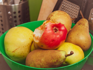 half-eaten Apple in a green bowl with other pears and apples