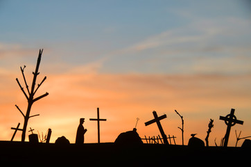 Fototapeta na wymiar Silhouette of decayed graveyard with tilted crosses and tombstones in sunset light.