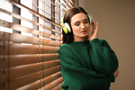 Young Woman Listening To Audiobook Near Window Indoors