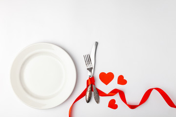 Romantic festive table setting on white background. Valentines day card template. Red ribbon, plate, silverware, vintage fork, knife. Concept anniversary, birthday, place for text, copyspace, top view