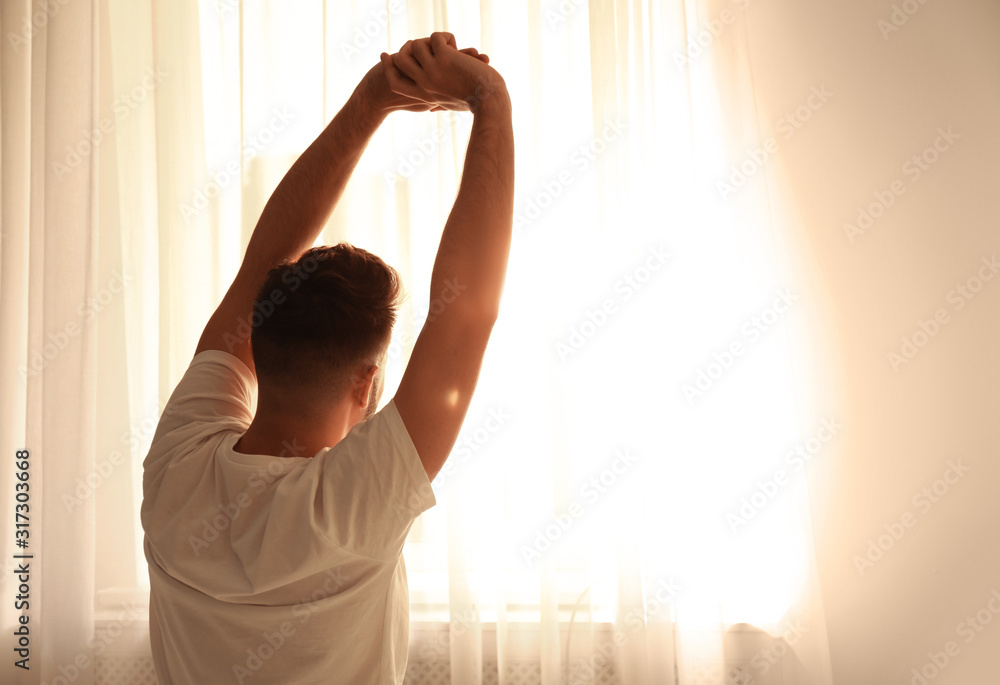 Sticker Man stretching near window at home, view from back. Lazy morning