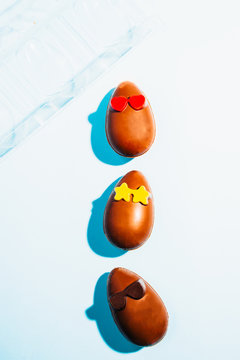 Funny chocolate eggs glasses, eaaster image with chocolate small eggs on a blue board, top view, flatlay with had directional light with deep shadows