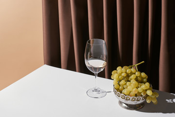 classic still life with grape and white wine on table near curtain isolated on beige