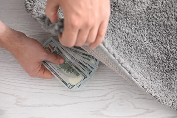 Man hiding money under carpet indoors, closeup. Financial savings