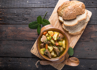 Irish dinner. Beef meat stewed with potatoes, carrots and soda bread on wooden background, top view, copy space. Homemade winter comfort food - slow cooked