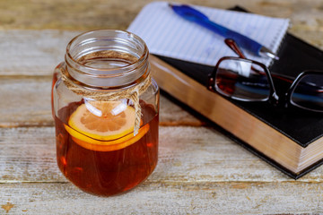 Book, pen, glasses and tea with lemon on table.