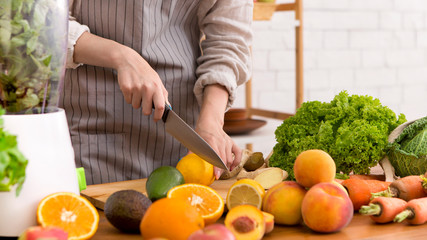 Unrecognizable woman cutting fruits and vegetables at kitchen