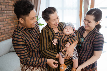 portrait of asian happy family wearing javanese batik heritage with sleeping son in the house