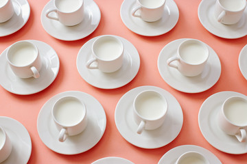 White cups filled with milk on pink background