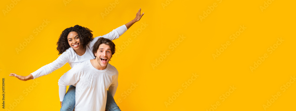 Wall mural Carefree interracial couple fooling and having fun together over yellow background