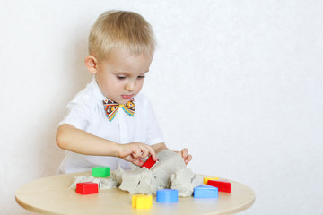 A 2-year-old toddler boy is playing with kinetic sand and colorful shapes, this activity develops fine motor skills in kindergarten children 