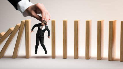 female hand drops a businessman as a stopper between falling domino-blocks on white background