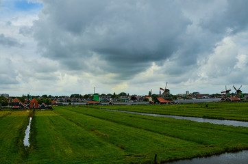 Fototapeta na wymiar Zaanse Schans, Holland, August 2019. North-east of Amsterdam is a small community located on the quay of the Zaan river. View from above of the fields with mills, tourists are noticed. Cloudy day.