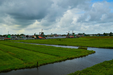Zaanse Schans, Holland, August 2019. North-east of Amsterdam is a small community located on the quay of the Zaan river. View from above of the fields with mills, tourists are noticed. Cloudy day.
