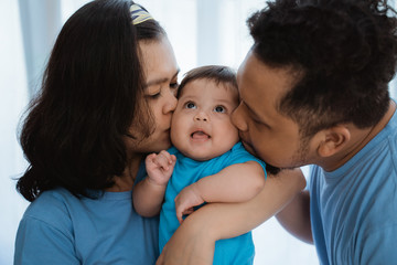 Asian little boy smiles when kissed by father and mother while joking