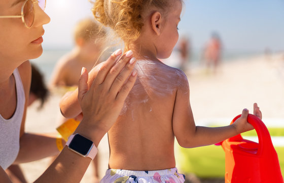 Caring mother apply sunblock to the back of her little daughter. Summer vacation sea beach