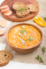 Sweet potato or batata cream soup with sesame seeds in a wooden bowl on a white wooden background. side view, close up.