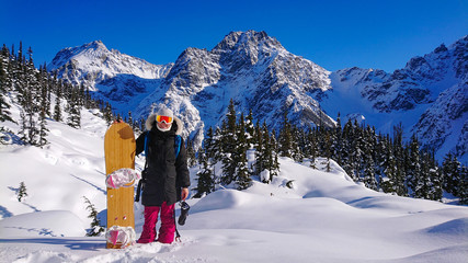 PORTRAIT: Cheerful female snowboarder smiles while posing in front of a mountain
