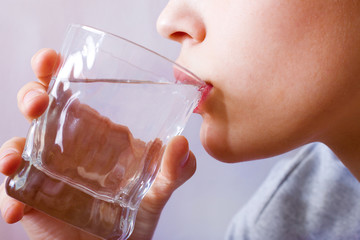A young girl drinks water from a glass glass. Concept of health, beauty, medicine. Drinking regime.