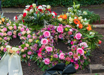 Viele bunte Kränze mit Schleifen auf einem Grab