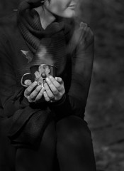 Black and white portrait, girl holds a hot mug of drink in her hands outdoors 